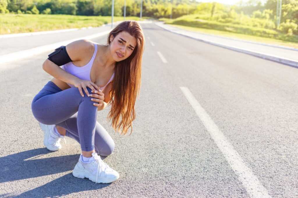 Young sports women having pain / injury during exercise and jogging in the nature. Female runner athlete leg injury and pain. Woman suffering from painful leg while running in the park.
